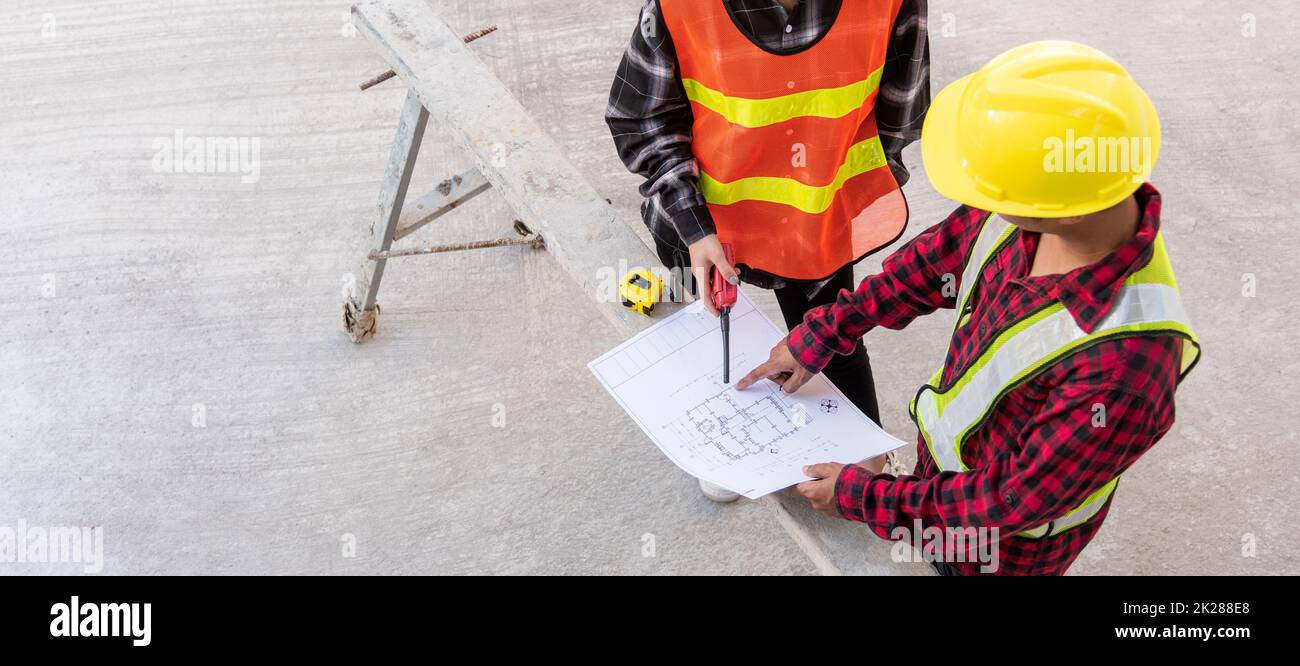 Architect and client discussing help create plan with blueprint of the building at construction site floor. Asian engineer foreman worker man and woman meeting and planning construction work, top view Stock Photo