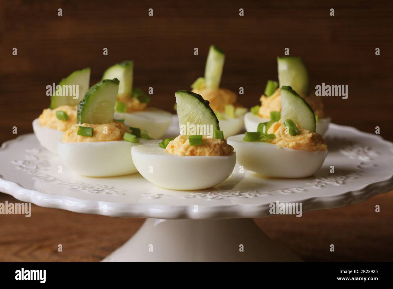 Spicy deviled eggs garnished with cucumber and leek on white plate