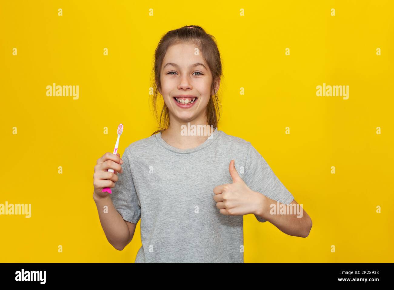 Beautiful brown-haired teenage girl holding brushing her teeth with toothbrush on a yellow background, Children nutrition and oral hygiene concept Stock Photo
