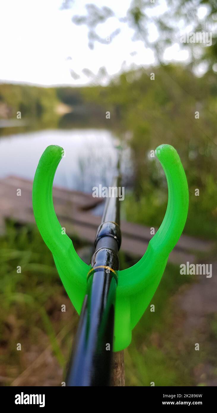 Fishing rod feeder on a stand against a lake. Close fishing on the river, fishing rod stands on a green slingshot Stock Photo