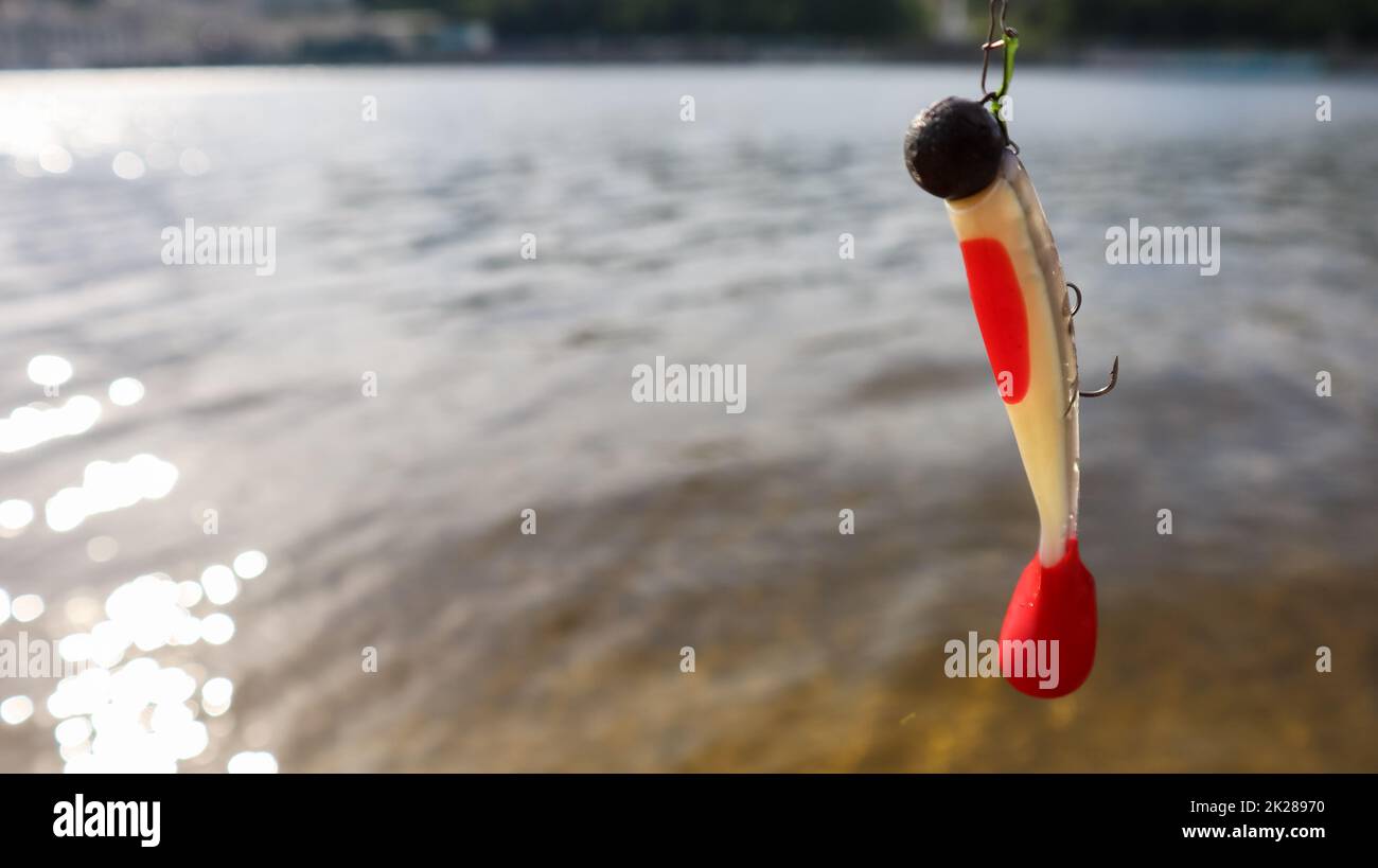 Ukraine, Kiev - June 2, 2020: Silicone fish wobblers hanging on a spinning rod, against the background of water. fishing lures for predatory fish. Copy space. Sport and hobbies Stock Photo