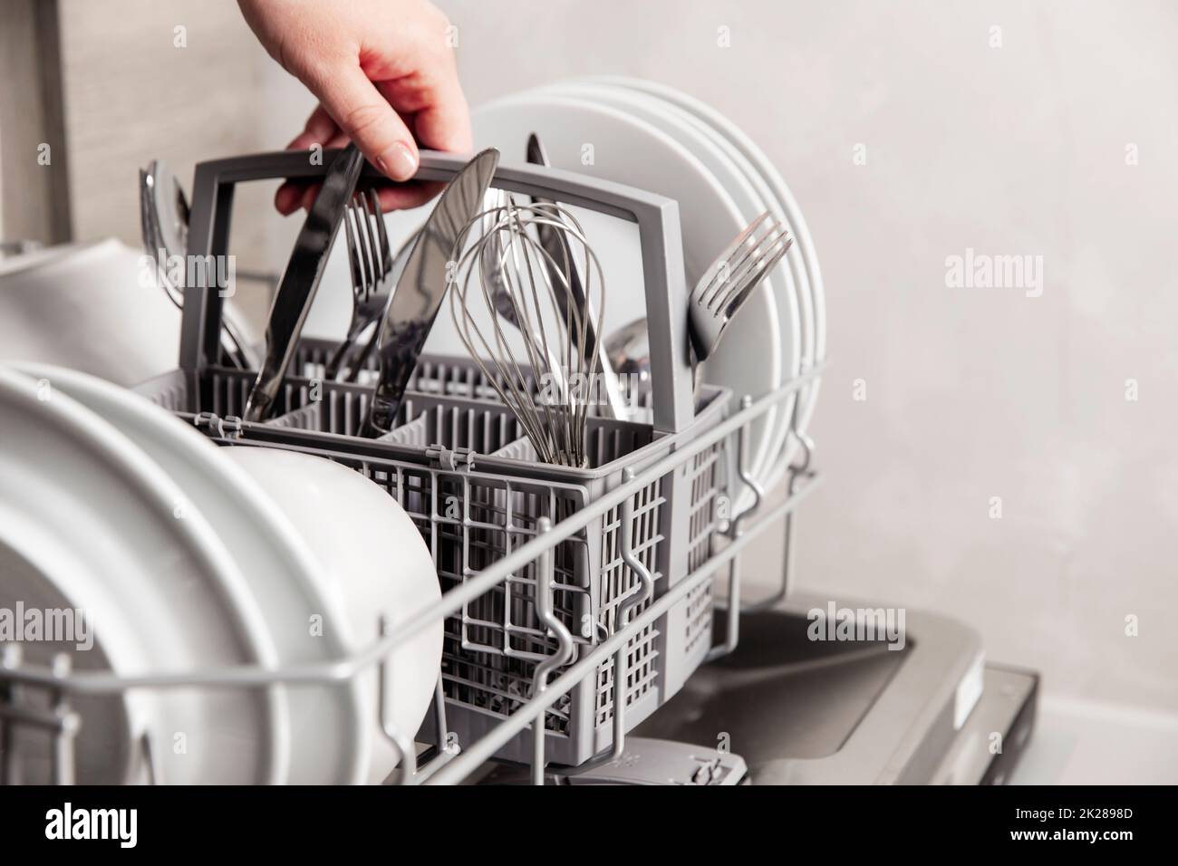 Hand holding box with clean cutlery in open dishwasher in the home