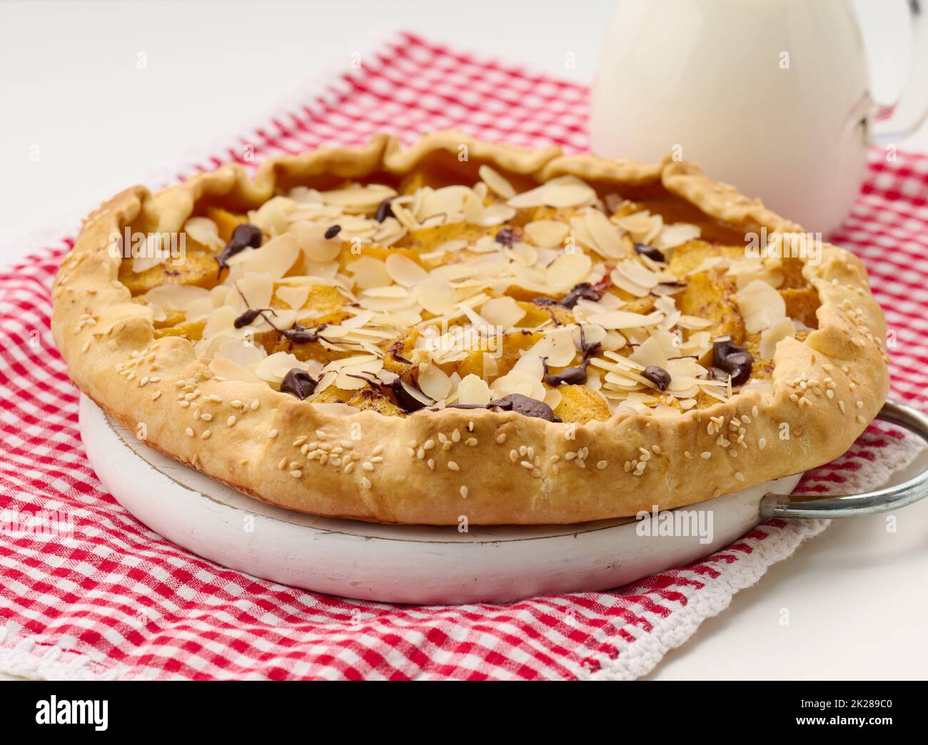 baked round pie with apple pieces, sprinkled with almond flakes on a white table Stock Photo