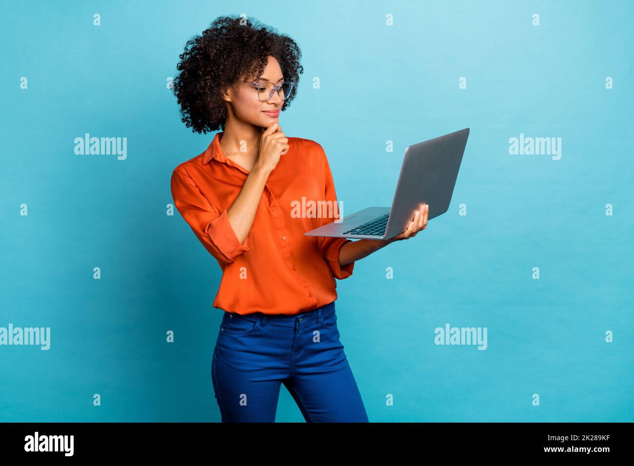 Portrait of beautiful trendy minded wavy-haired girl using laptop analyzing isolated on vivid blue color background Stock Photo