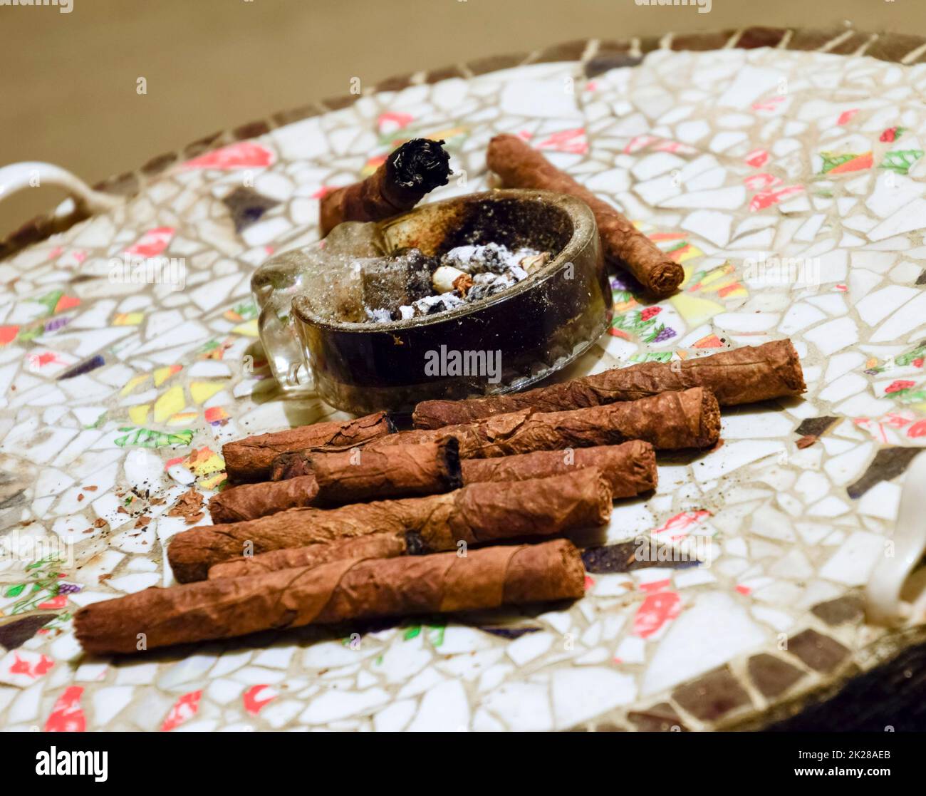 Cigar and ashtray on the table of the glued pieces of pottery. Homemade cigars from leafy tobacco leaves on a ceramic table. Ashtray and cigars. Stock Photo