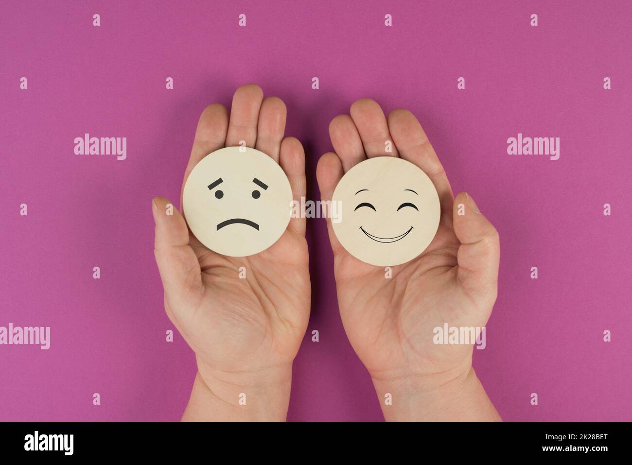 Holding two wooden circles in the hands one face is sad the other one is smiling, porsitive and negative emotions, rating concept, choosing the mood Stock Photo