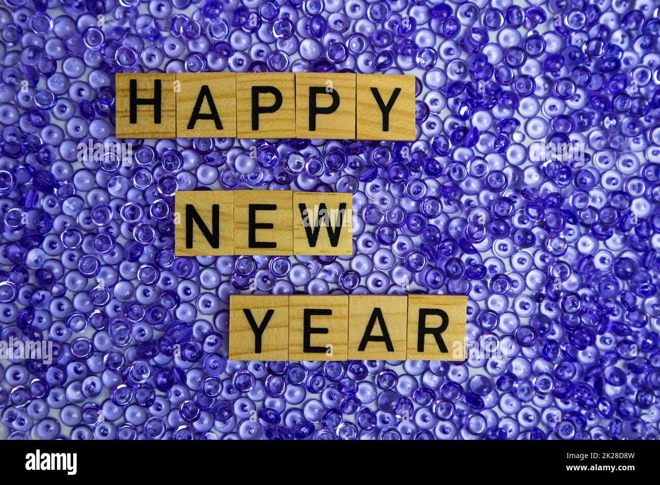 Text Happy New Year from wooden letters on a purple pearl background. Stock Photo