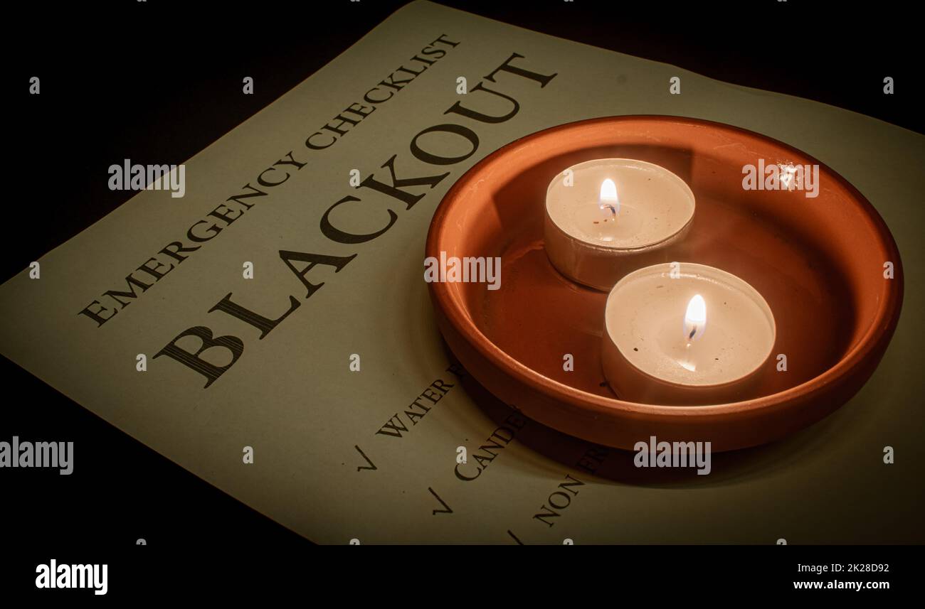 two tea lights in a terracotta coaster on a blackout emergency checklist during a power outage Stock Photo