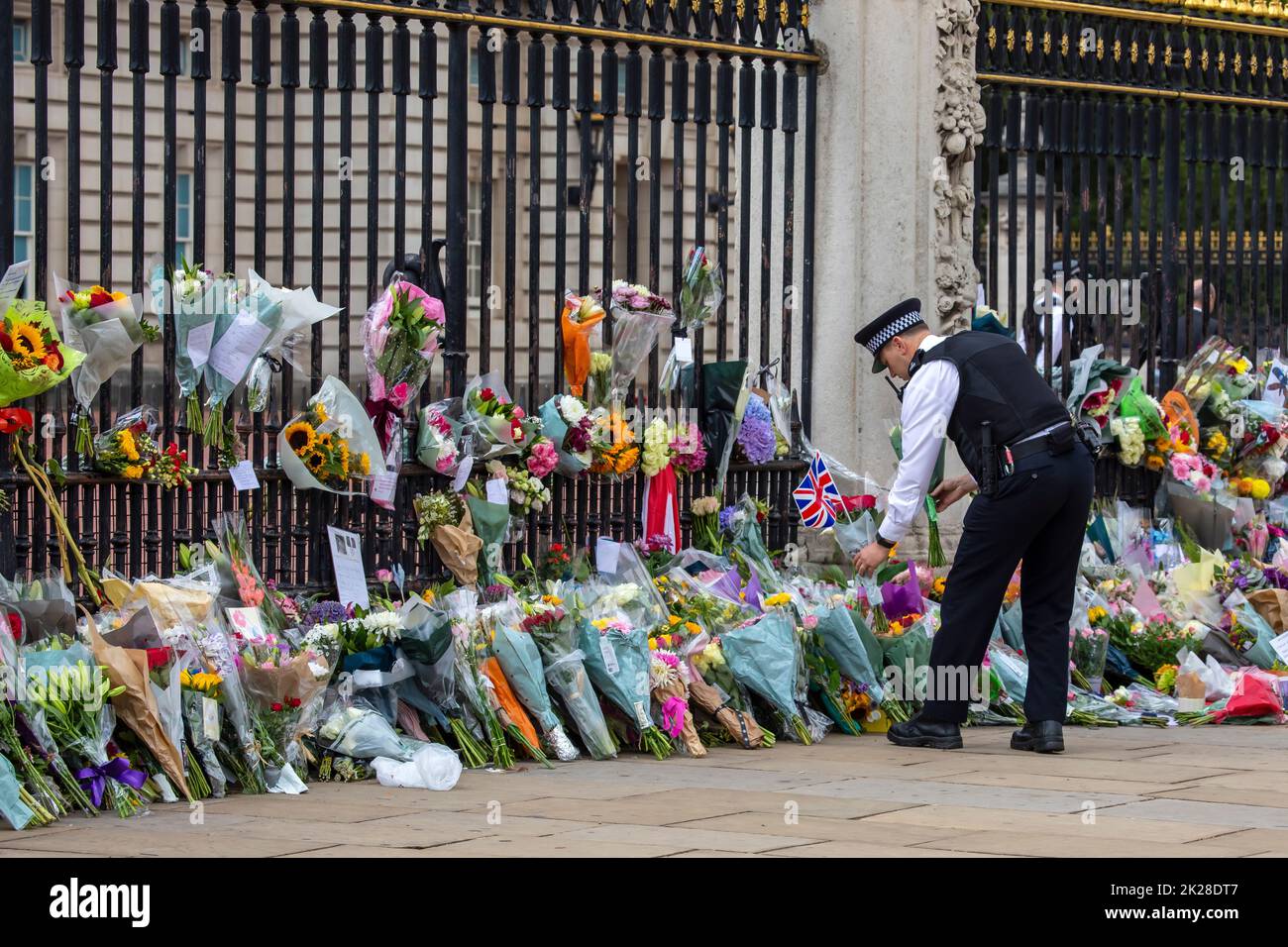 London, UK - September 9th 2022: A policeman placing flowers in front of the gates at Buckingham Palace in London, in commemoration of Queen Elizabeth Stock Photo