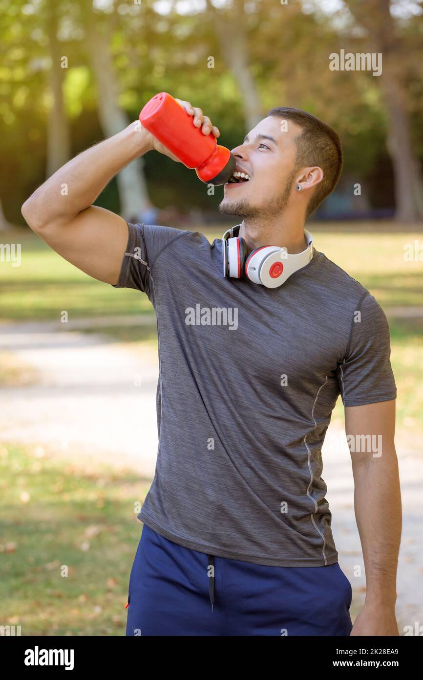 Runner smiling young latin man drinking water running portrait format sports training fitness workout Stock Photo