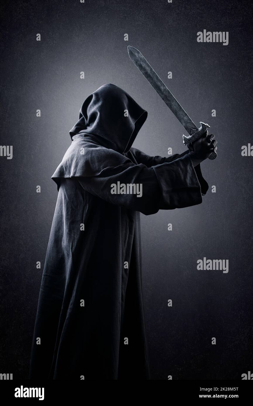 Warrior with hooded cape and medieval sword over dark misty background Stock Photo