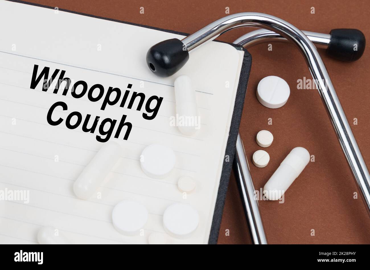 Medical concept. On a brown surface lies a stethoscope, pills and a notepad with the inscription - Whooping Cough Stock Photo