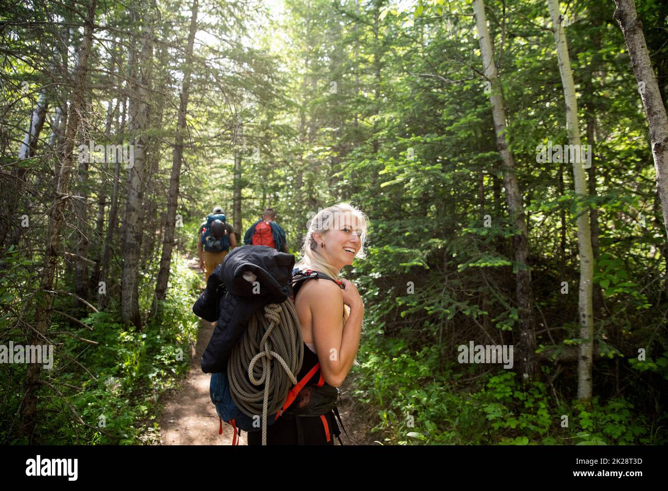 Smiling young woman hiking with climbing gear among trees in woods