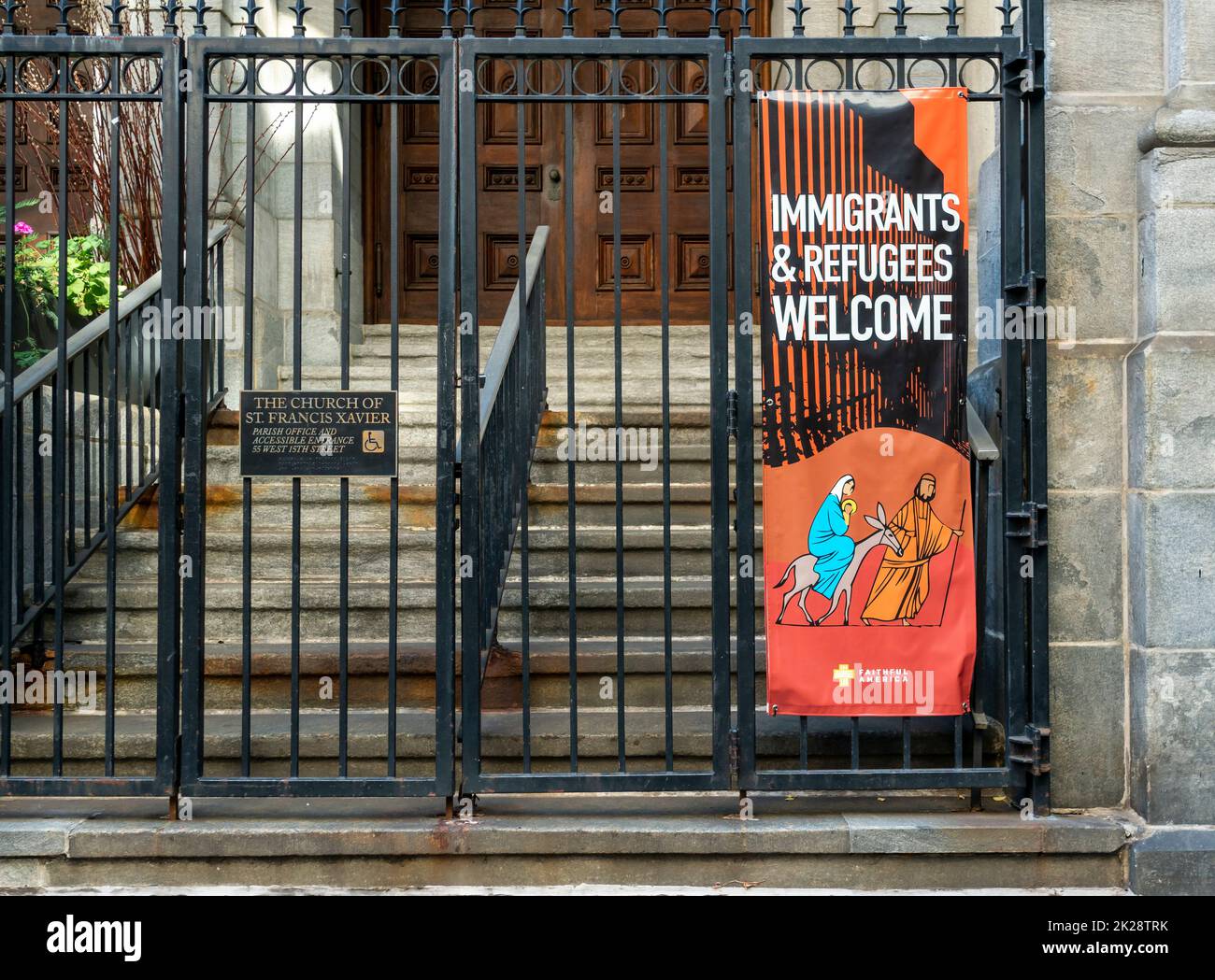 A sign hanging on the fence of the Church of St. Francis Xavier in the Chelsea neighborhood of New York on Thursday, September 15, 2022 welcomes immigrant and refugees. (© Richard B. Levine) Stock Photo