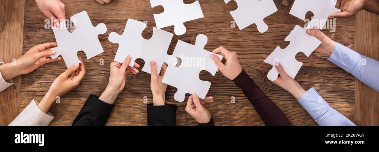 Overhead Teamwork Meeting Solving Jigsaw Puzzle At Desk Stock Photo