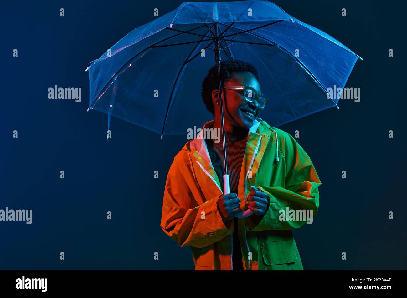 Hipster woman in raincoat with umbrella in neon light Stock Photo