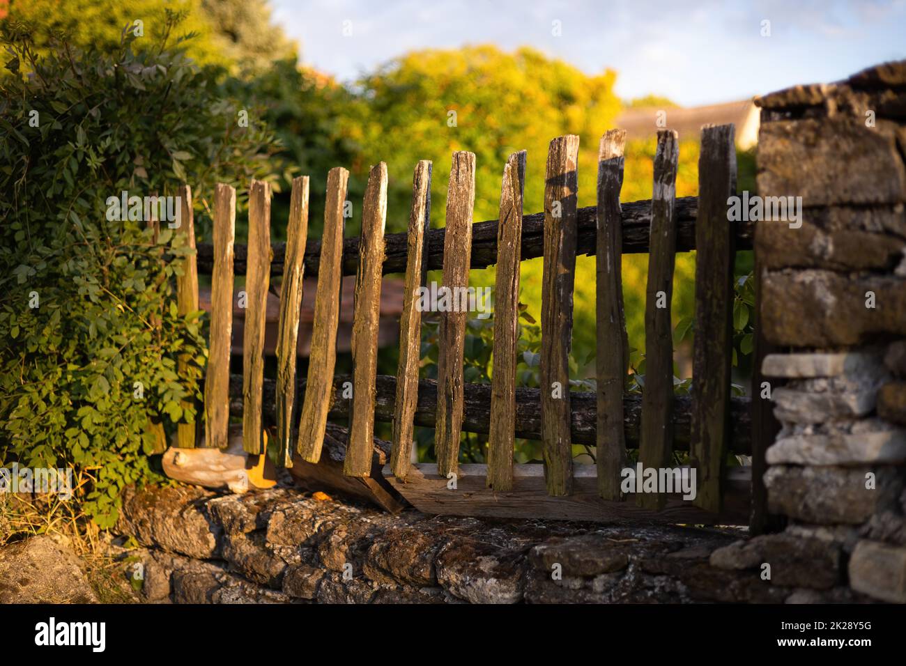 Old wooden picket fence built into a wall from stones. Stock Photo