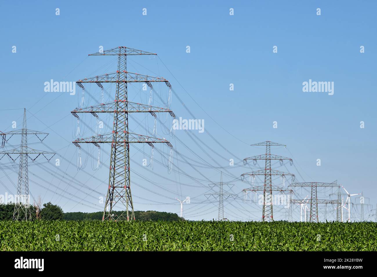 Electricity pylons and power lines with wind turbines in the back seen in Germany Stock Photo