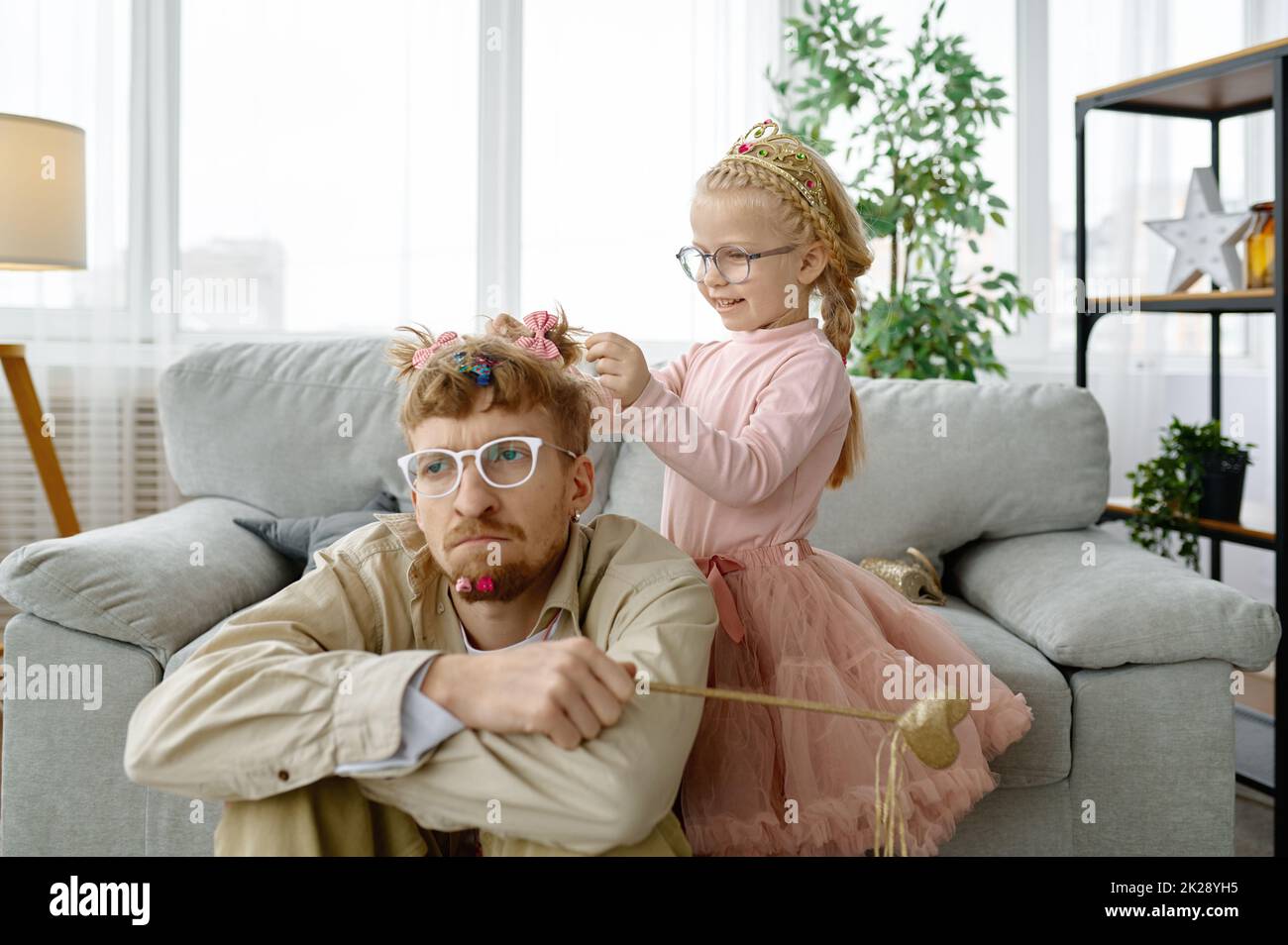 Cute daughter making hairstyle for exhausted father Stock Photo
