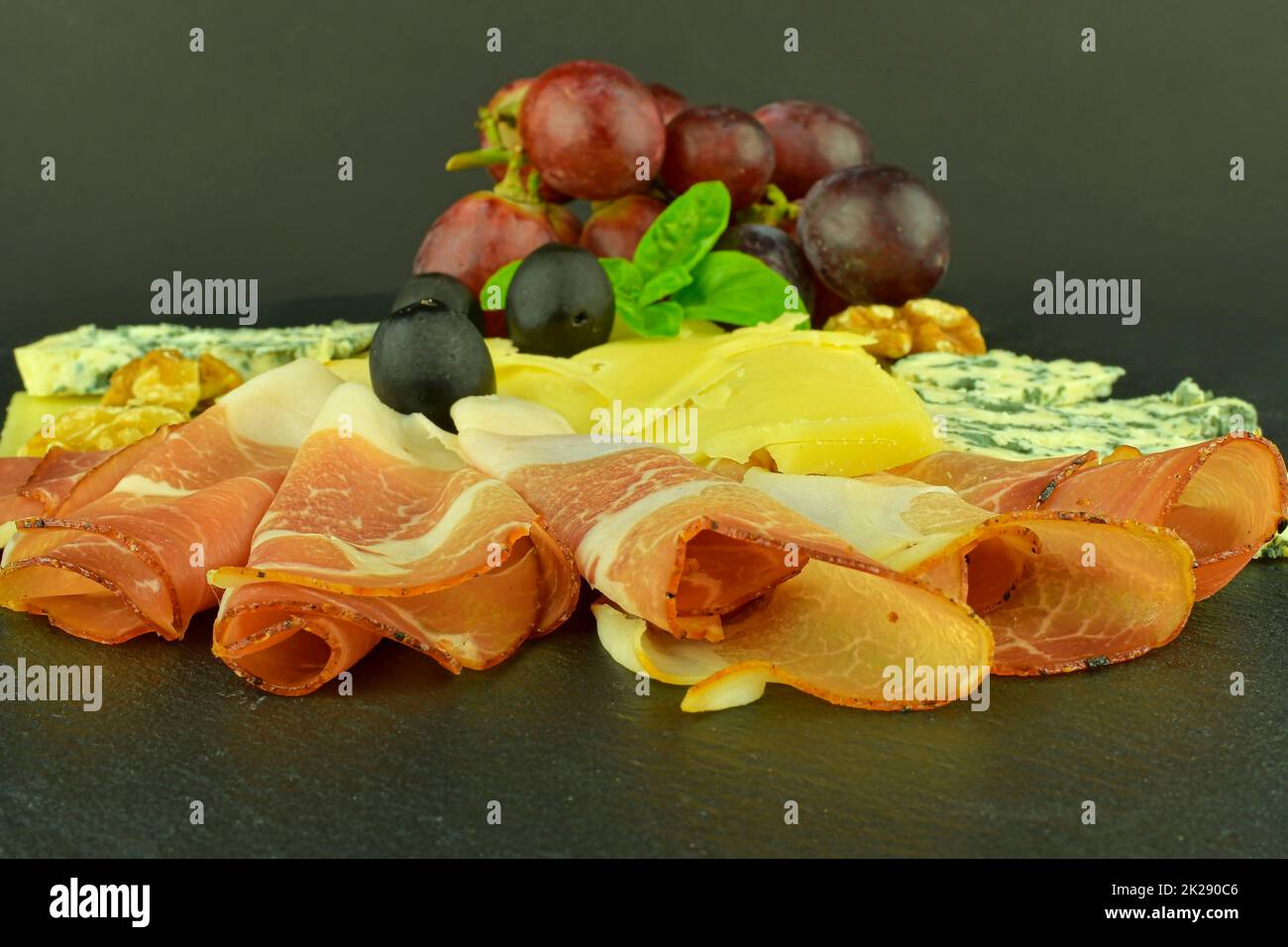 Assorted cheeses on black slate board. Brie cheese, cheddar slices, walnuts, grapes, olives and