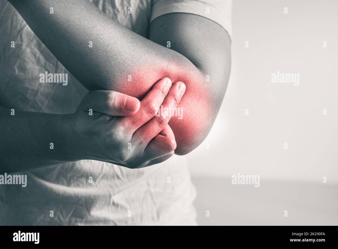 Elbow injury from tennis and golf. The man uses fingers to massage his arm. Pain symptom area is shown with red color. Healthcare knowledge. Medium close up shot with copy space. Black and white tone. Stock Photo