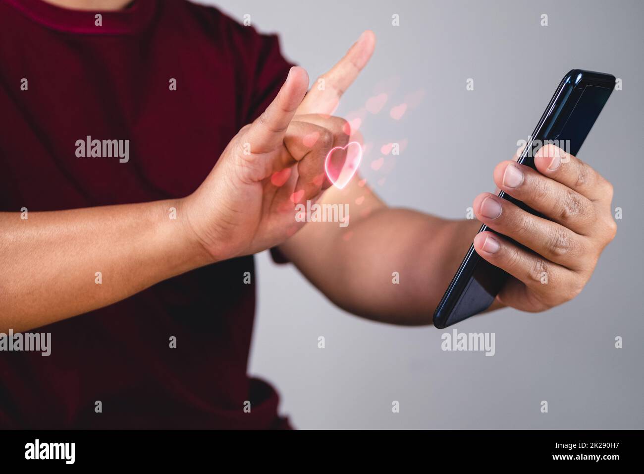 Valentine's day concept. Person uses hand to give love thru a smartphone. Heart shape in visual effect. Stock Photo
