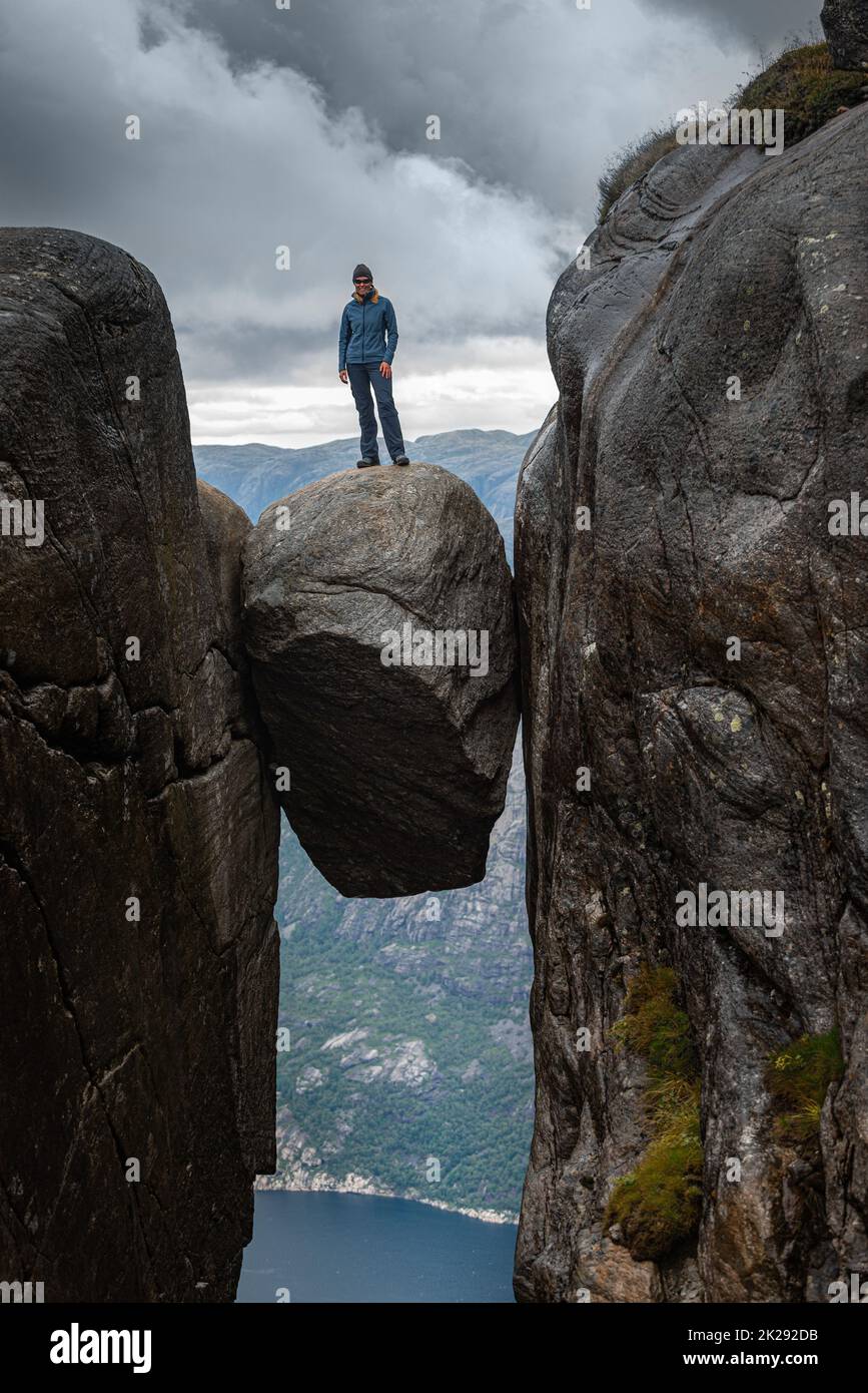 Woman stands on top of large boulder, Visiting Norway Kjeragbolten located south of Lysefjorden Stock Photo