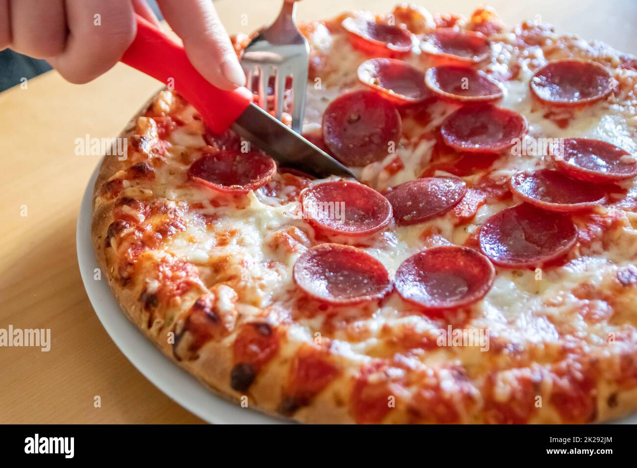 Boy hands cut salami pizza into pieces with fork and knife on pizza