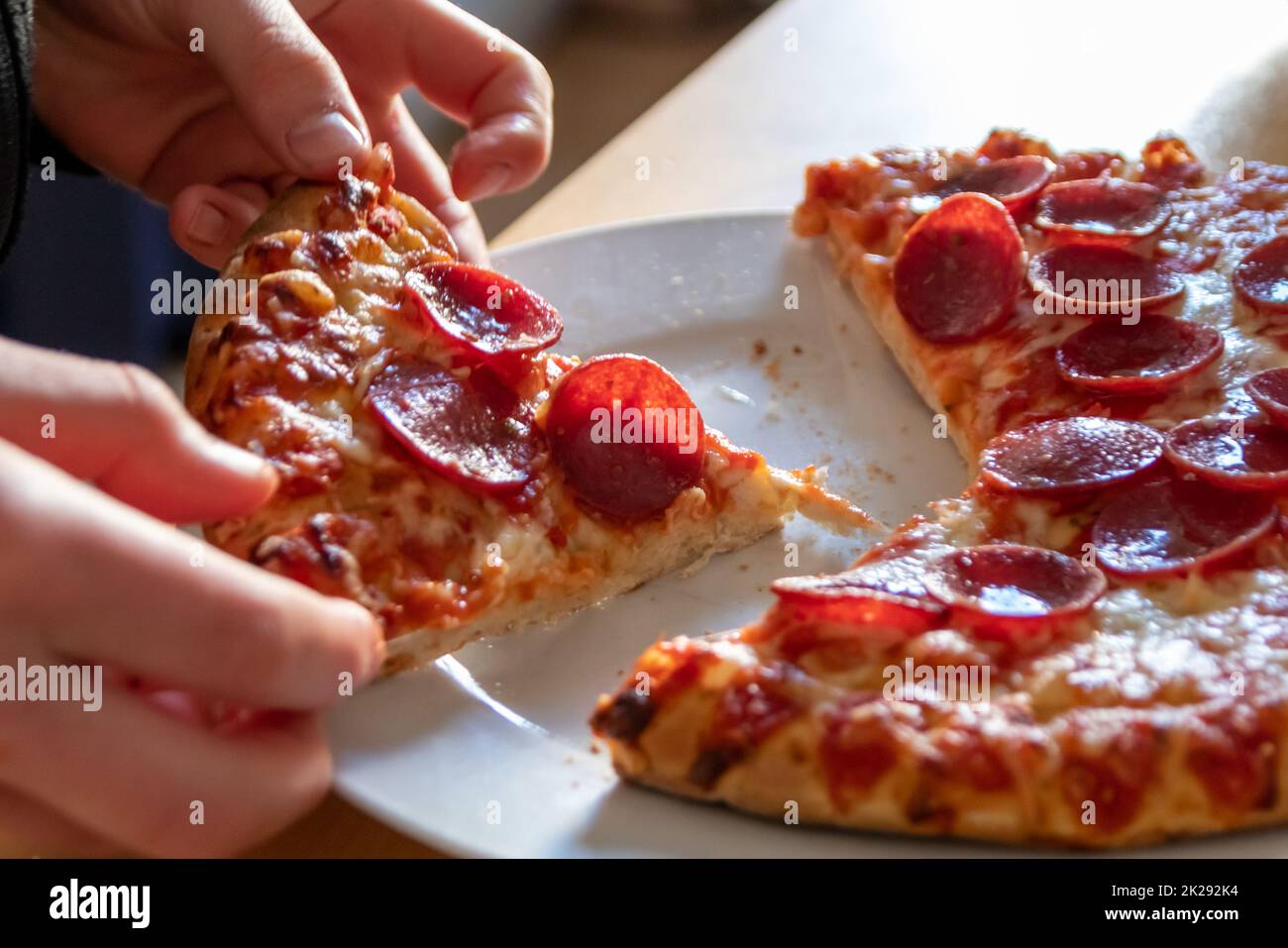 Child hand holding piece of pizza salami with hot steam and delicious cheese eating joyful the