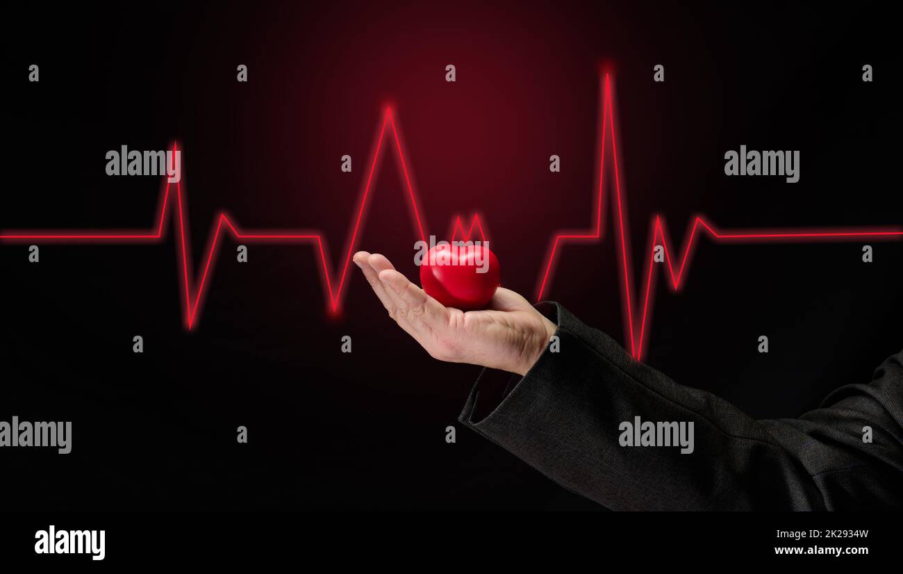 Male hand holding a red heart on a dark background, early diagnosis of the cardiovascular system Stock Photo