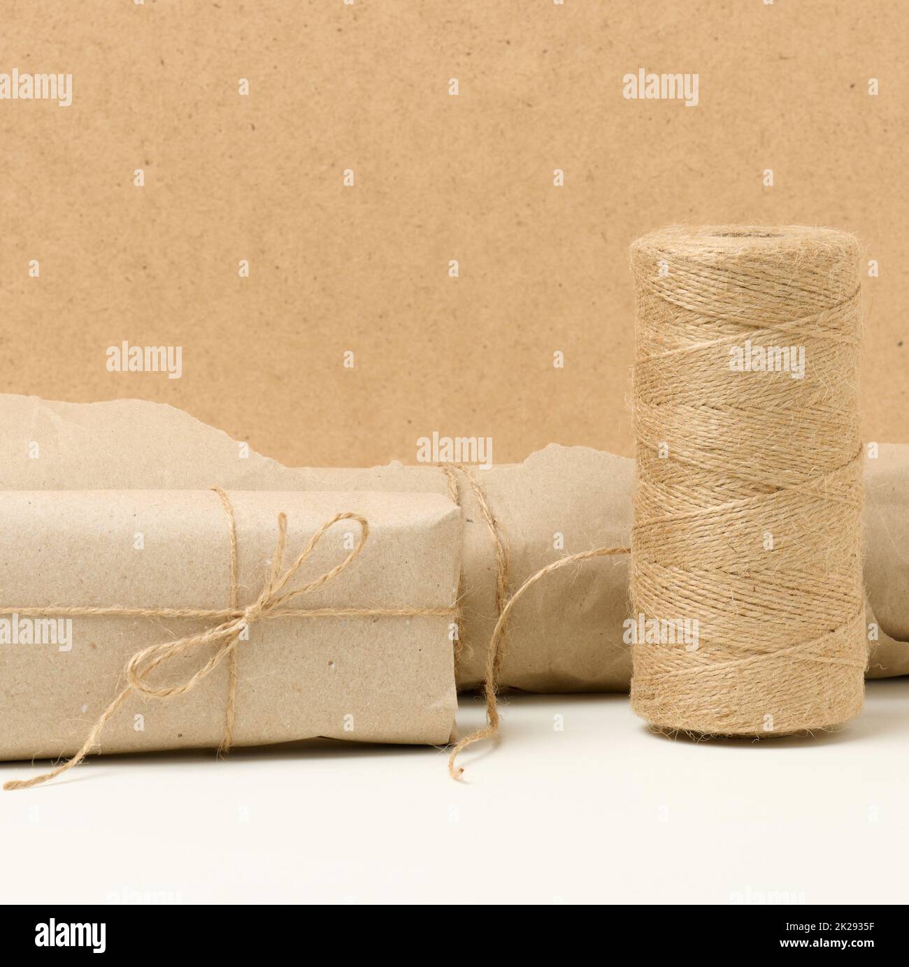 box, roll of brown kraft paper and reel with brown rope on white table, packing material Stock Photo