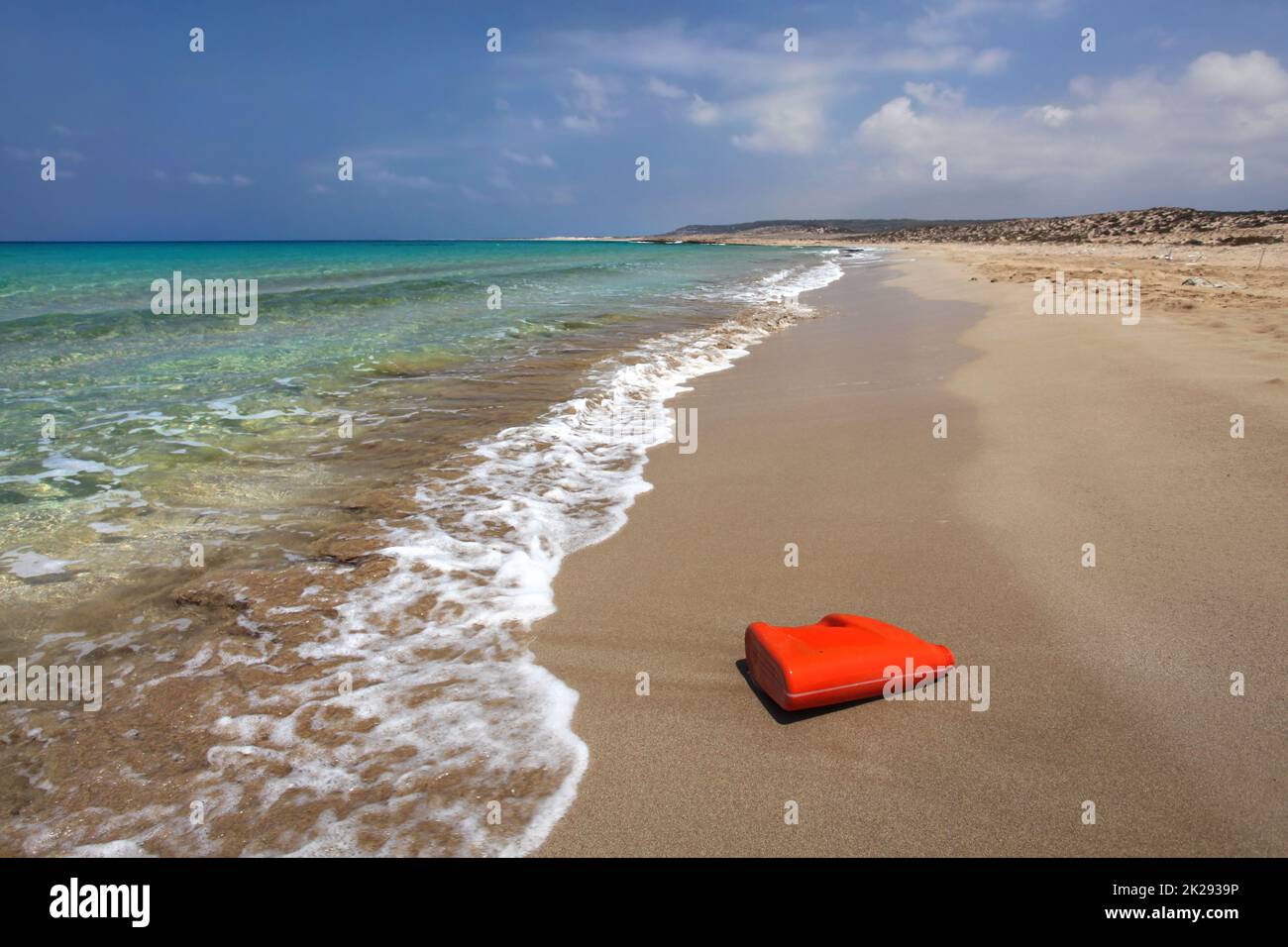 Bright red plastic oil (or washing liquid) container on beautiful unspoiled beach. Sea plastics littering concept. Karpazz, Northern Cyprus. Stock Photo