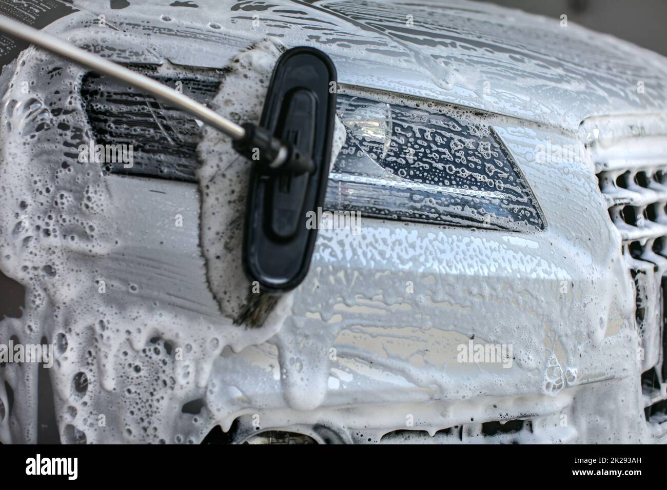 Front light of silver car washed in self service carwash. Brush leaving strokes in shampoo and foam Stock Photo