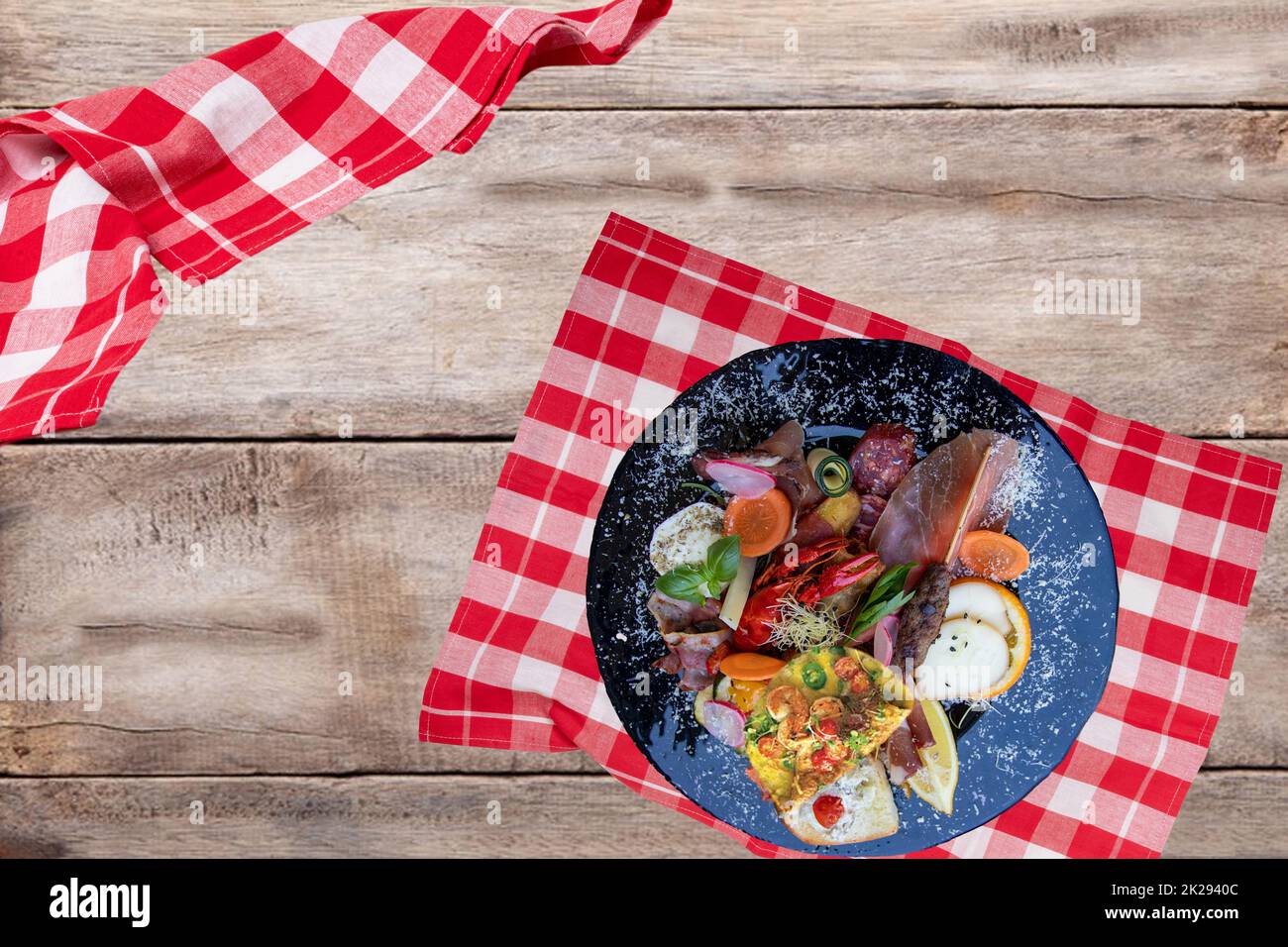 Traditional italien food. Closeup of mixed mediterranean appetizers or antipasto and tapas with ham vegetables and cancer on a black plate on a rustic wooden table. Top view. Stock Photo