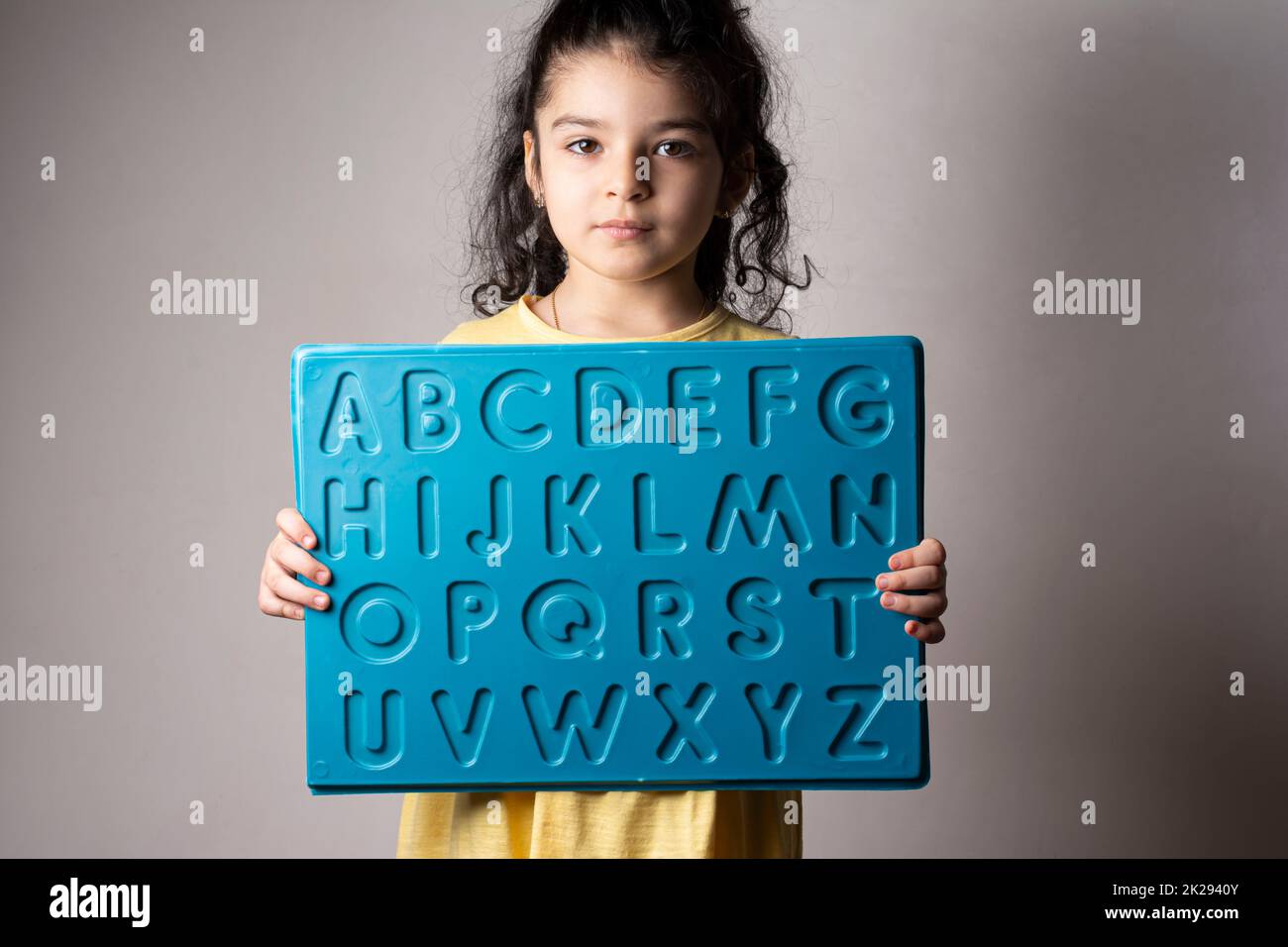 Little girl with yellow dress holding an English letters sheet in hands Stock Photo