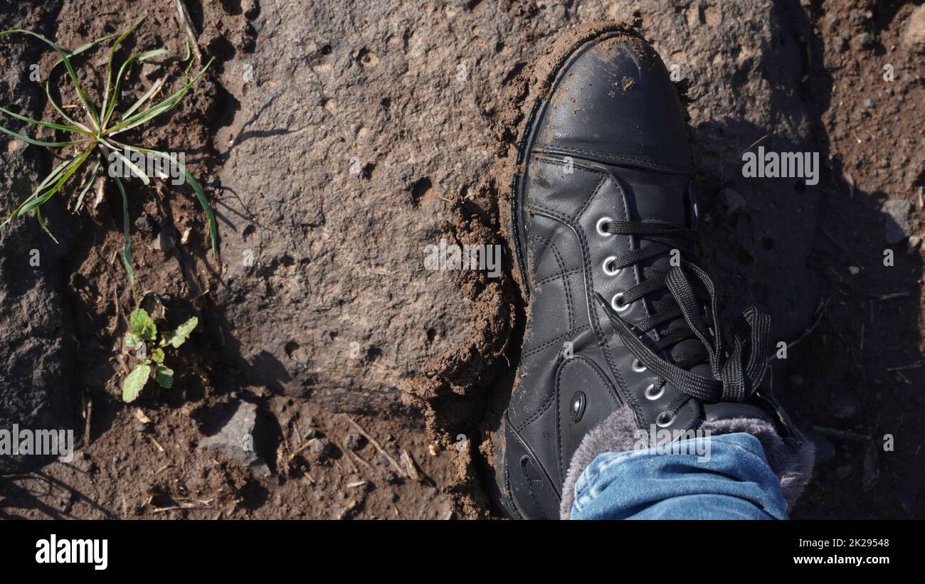 Women boots in the mud, detail of dirty boots and muddy, walk. Top down dirty black laced boots woman in blue jeans. Stock Photo