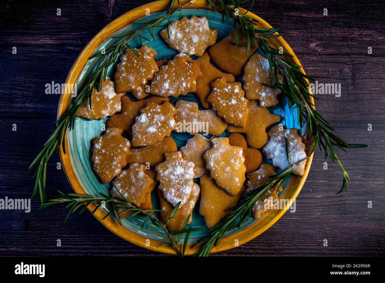 Cookies in the form of Christmas trees lie on a blue plate, decorated with rosemary on the sides on a dark background Stock Photo