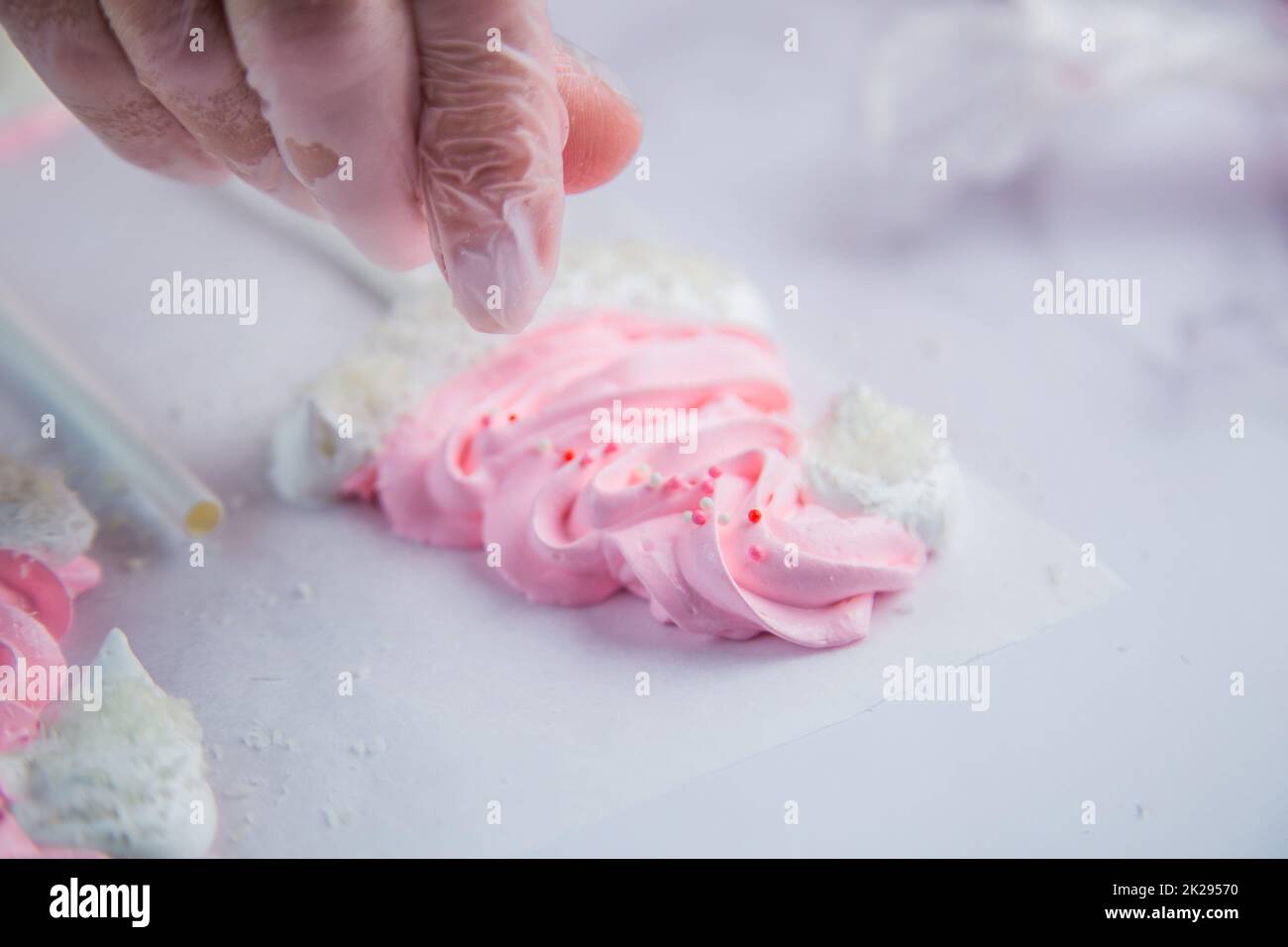 Pink meringue hats with white pompoms and brims are sprinkled with white balls on the side, against a parchment background Stock Photo