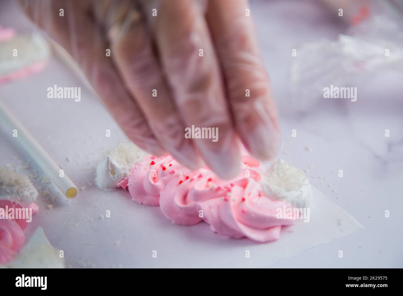 Pink meringue hats with white pompoms and brims are sprinkled with white balls on the side, against a parchment background Stock Photo