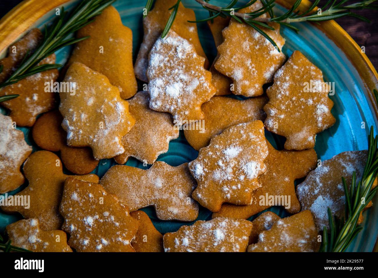 Cookies in the form of Christmas trees lie on a blue plate, decorated with rosemary on the sides on a dark background Stock Photo