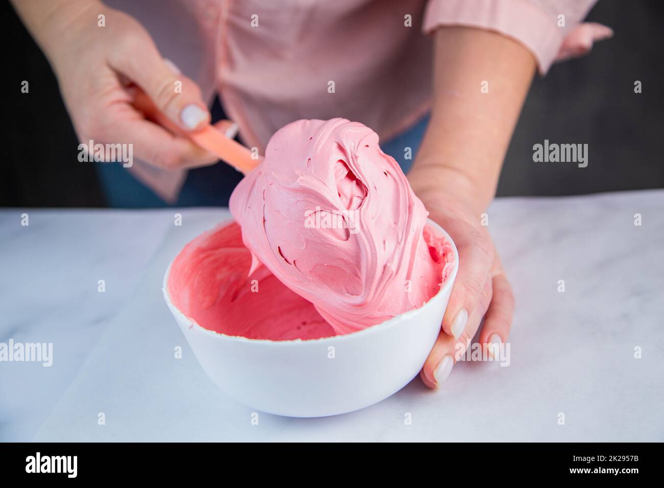 Pink confectionary meringue marengo is mixed in a white bowl on a white marble background by the hands of a pastry chef Stock Photo