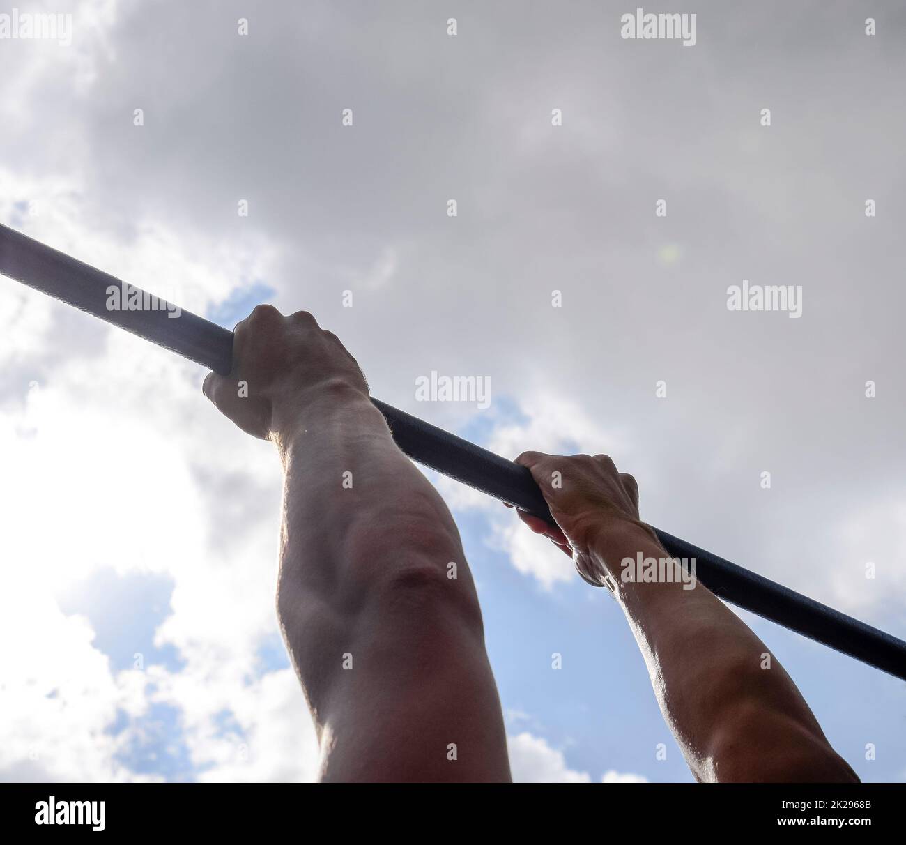 Hands on the bar close-up. The man pulls himself up on the bar. Playing sports in the fresh air. Horizontal bar. Stock Photo