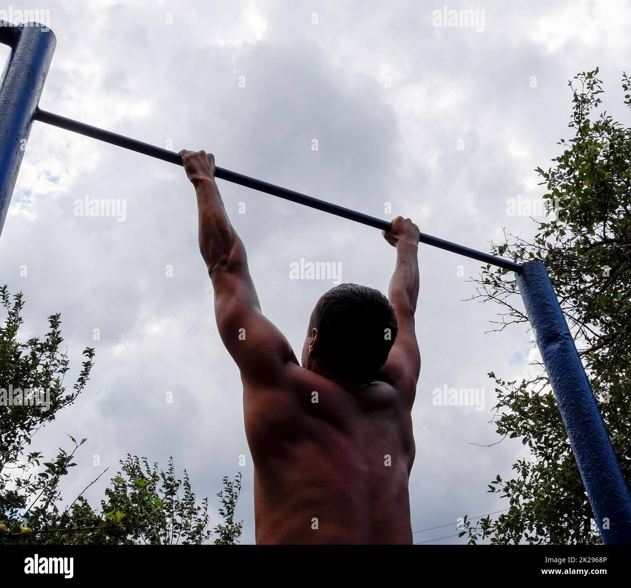 The man pulls himself up on the bar. Playing sports in the fresh air. Horizontal bar. Stock Photo