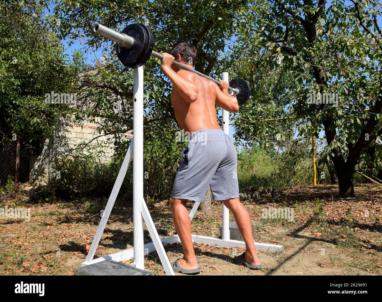 man takes a bar to perform squats. Exercises in bodybuilding. sport in the backyard. Stock Photo