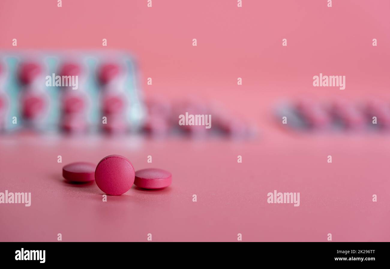 Round pink tablet pill on blur blister pack. Prescription drug. Painkiller or antibiotic tablet pill on pink background. Pharmaceutical industry. Health and wellbeing background. Pharmaceutics concept Stock Photo