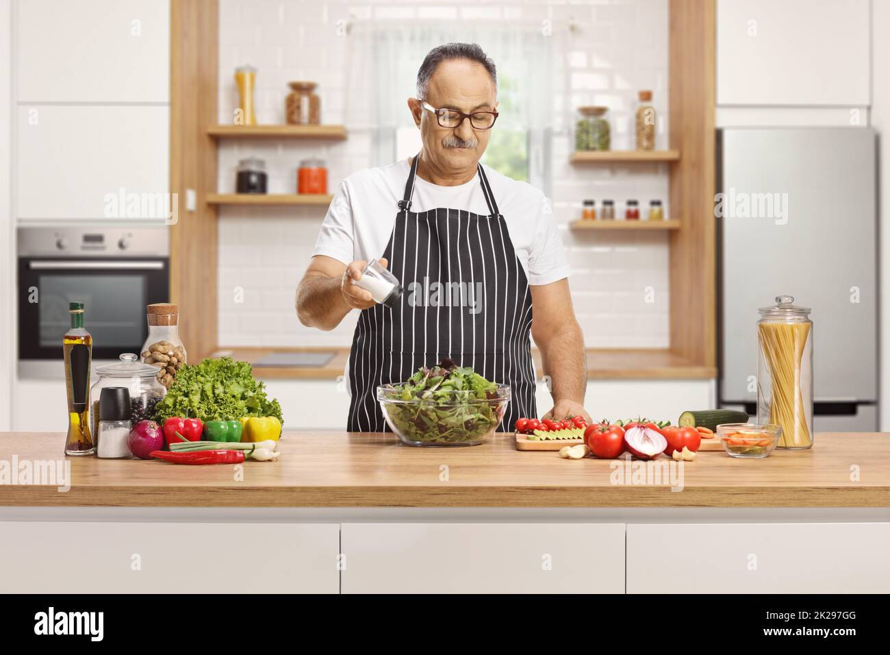 Mature man with an apron seasoning a salad with salt on a kitchen counter Stock Photo