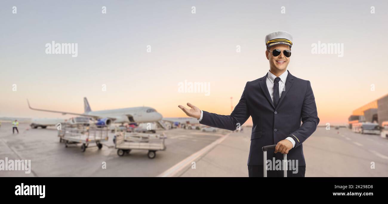 Pilot standing with a suitcase on an airport with plane in the background and pointing with hand Stock Photo