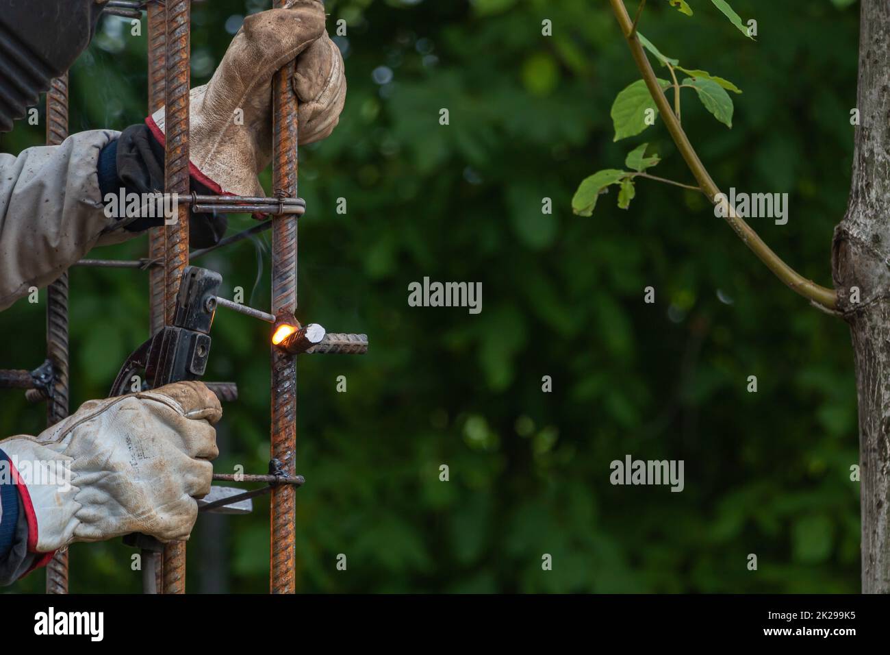 A worker welds a reinforcement - future column - construction concept. Green trees background Stock Photo