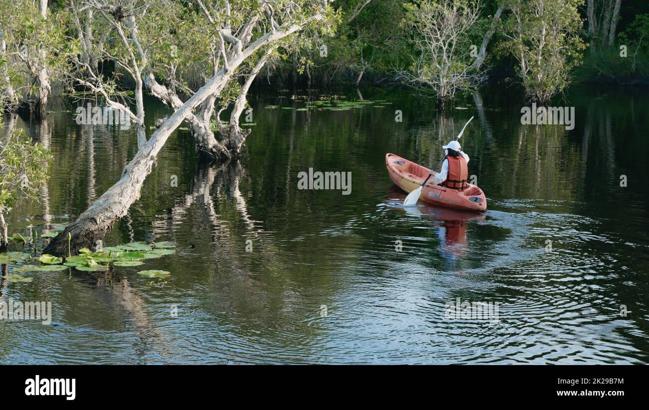 Back young adult woman paddling kayaking canoe on a lake on summer day Stock Photo