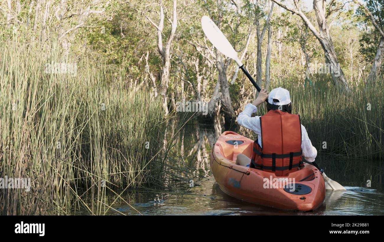 Back young adult woman paddling kayaking canoe on a lake on summer day